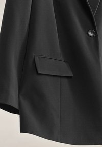 Blazer nero realizzato in tessuto testurizzato, con chiusura a un bottone e tasca a falda sul lato sinistro.