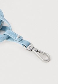 Svetlomodrý kožený remienok s bielym prešitím pripevnený k striebristému kovovému karabínovému klipu na bielom pozadí.