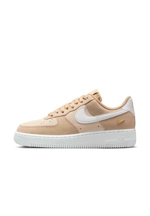 Beige Nike Air Force 1 sneaker med hvid sål, hvid Nike swoosh og lille guld swoosh nær hælen på hvid baggrund.