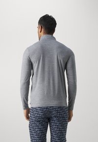 Pilkas ilgomis rankovėmis polo, su apykakle, pagamintas iš tekstūruoto trikotažo. Su tartuota kelnėmis, ant kurių matomas mėlynas "Calvin Klein" logotipas.