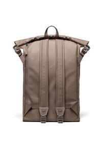 Sac à dos à rabat en matériau beige mat, avec des bretelles rembourrées, une poignée supérieure et des doubles zippers avec matériel réglable pour une fermeture sécurisée.