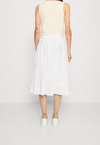 Falda midi blanca con un diseño fluido, combinada con un top ajustado de color beige claro. El conjunto presenta una textura suave y siluetas simples.