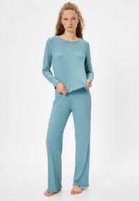 Conjunto de loungewear de color azul claro, con textura acanalada, que incluye una camiseta de manga larga y pantalones a juego con bordes sin terminar y un ajuste relajado. Textura suave.