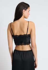 Camisole en satin noir avec dentelle, bretelles spaghetti ajustables, design ajusté et texture lisse, assortie à une jupe coordonnée.