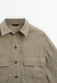 Beige linned skjorte med krave, to brystlommer og træknapper, med en struktureret stof og løs pasform.