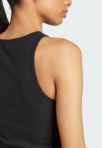 Čierny rebrovaný tielko s okrúhlym výstrihom, s priliehavým strihom a stredne širokými ramienkami, zobrazené zozadu. Mäkká textúra.