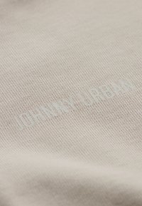 Világos bézs szövet, textúrált szövésű; kiemelkedő, domború "JOHNNY URBAN" felirattal világoskék színben.