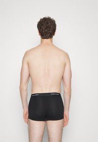 Juodi medvilniniai bokseriai su Calvin Klein logotipu, prigludęs dizainas ir lygi tekstūra, matomi iš nugaros.