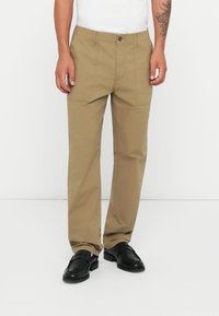 Beige színű pamut nadrág egyenes lábformával, oldalzsebekkel és gombos záródással. Fekete bőrcipővel viselve.