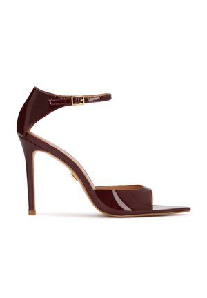 Sandale à talon haut en cuir verni bordeaux foncé avec bride à la cheville et boucle dorée, bout ouvert et talon aiguille fin.