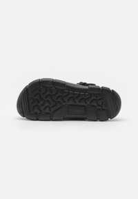 Sole di scarpa nera con un motivo di grip testurizzato, tacco arrotondato e area della punta rinforzata. Il materiale sembra gomma con un design piatto.
