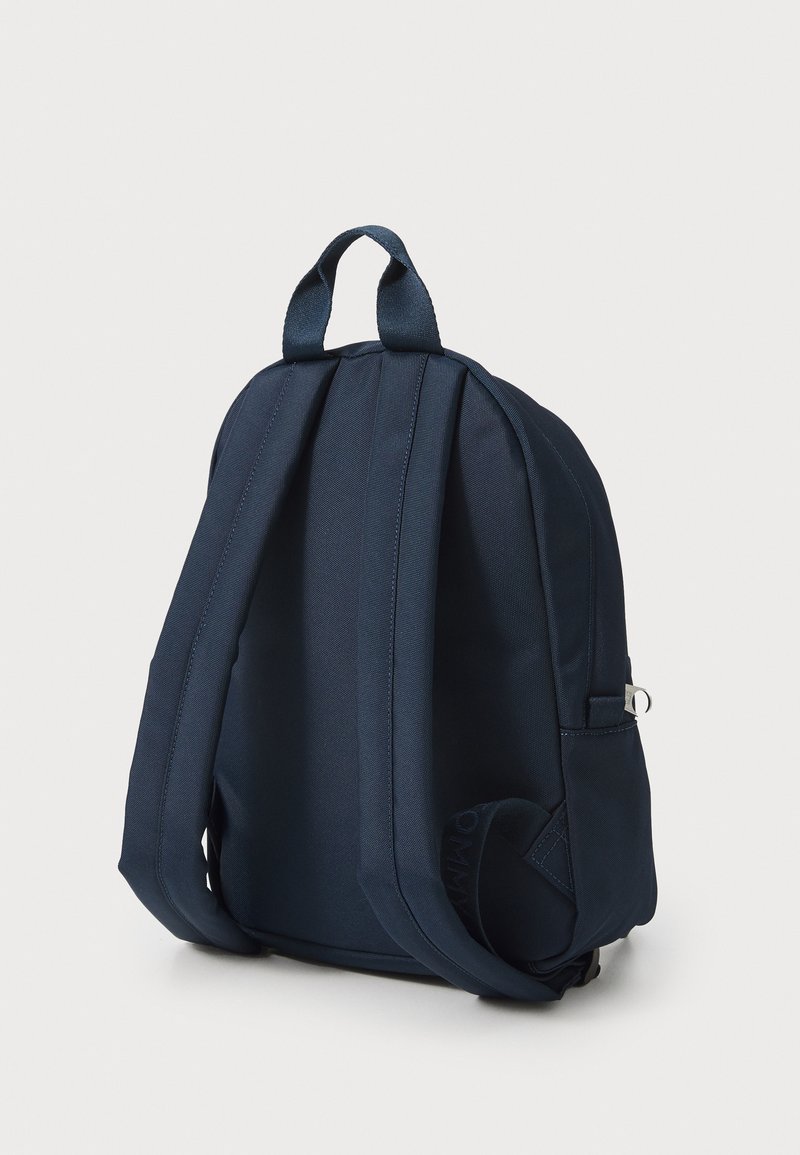 Granatowy plecak z tkaniny z wyprofilowanymi, wyściełanymi ramiączkami, uchwytem na górze i minimalistycznym designem. Ma boczną kieszeń z metalowym akcentem.