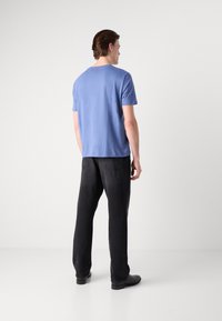 Light blue short-sleeve t-shirt and black jeans, viewed from the back. Soft fabric, relaxed fit, and minimalistic design. Black footwear.