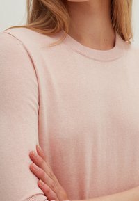 Jasnoróżowy sweter dziany z okrągłym dekoltem, krótkimi rękawami i subtelną fakturą, o dopasowanym kroju i miękkim materiale.