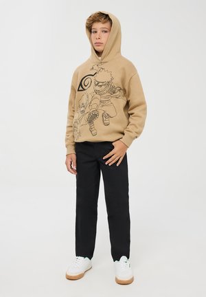 Felpa beige con grafica a fumetti nera, abbinata a pantaloni neri e sneakers bianche con suola marrone.