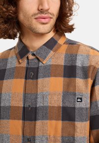 Bruine en grijze geruite overhemd met knopen, gemaakt van een gestructureerde stof, met een kraag, een borstzak en een klein logopatch op de borst.