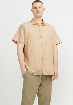 Chemise à manches courtes avec boutons en tissu pêche clair, offrant une coupe décontractée, une texture douce et un col pointu. Associée à un pantalon kaki.