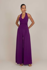 Tuta a halter viola con busto aderente, gambe ampie plissettate e tessuto morbido. Orecchini con accento dorato completano il design.
