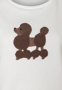 Weißes Kleidungsstück mit einem braunen Frottéestoff und gesticktem Pudel-Design, das strukturierte Fell-Details sowie einen runden, flauschigen Schwanz und Ohren aufweist.