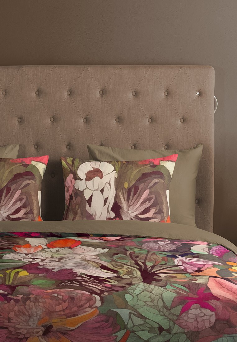 Bettwäsche mit floralem Muster, das ein farbenfrohes Design in Rosa-, Grün- und Orangetönen zeigt, kombiniert mit einfarbigen taupefarbenen Kissen und einem gepolsterten Kopfteil.