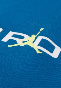 Μπλε ύφασμα με λευκά γράμματα και ένα κίτρινο σιλουέτα γραφικό ενός άλματος, τοποθετημένο σε ένα υφασμένο φόντο.