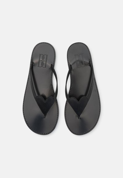 Chanclas de cuero negro con un diseño en forma de corazón en el empeine, suela plana y costuras en contraste. Textura suave en toda la superficie.