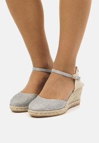 Sandali con zeppa in glitter argento, cinturino alla caviglia, piattaforma avvolta in juta, punta rotonda e decorazione con fibbia.