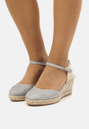 Sandali con zeppa in glitter argento, cinturino alla caviglia, piattaforma avvolta in juta, punta rotonda e decorazione con fibbia.