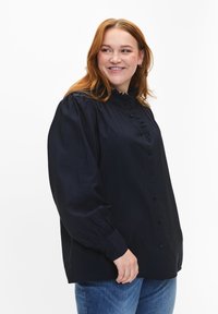 Tumesinine nupuga särk, millel on volangiga krae ja nööpide rida. Iseloomustab pikad, täiskäised koos kokku tõmmatava detailiga ja vabam lõige.