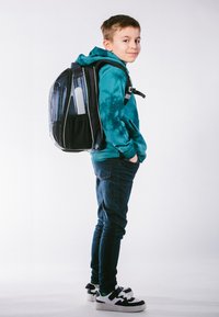 Schwarzer und grauer Rucksack mit Netzakzenten, getragen von einem Jungen in einem türkisfarbenen Hoodie und blauen Jeans, mit einem schlanken Design und verstellbaren Trägern.