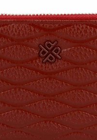 Nahaufnahme eines roten Lederportemonnaies mit geflochtenem Muster, geprägtem vierbuchstabigen Logo in der Mitte und rotem Reißverschluss am oberen Rand.