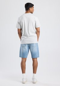 Lichtgrijs katoenen t-shirt, losse pasvorm, gecombineerd met lichtblauwe denimshorts. Witte sokken en witte sneakers maken de casual look compleet.
