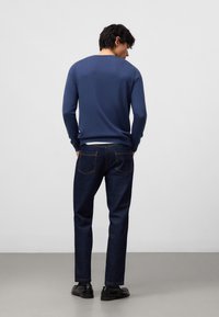 Dunkelblaues Strickpullover mit Rundhals, kombiniert mit dunkelblauen Jeans. Die Jeans haben ein klassisches Fünf-Taschen-Design. Schwarze Schuhe vervollständigen den Look.