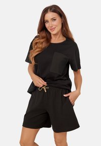 Czarny bawełniany t-shirt z teksturowaną kieszenią, w połączeniu z czarnymi dzianinowymi szortami z elastycznym pasem i dekoracyjnym sznurkiem.