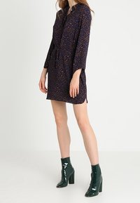 Granatowa sukienka w kwiatowy wzór, z długimi rękawami, zapinana na guziki z paskiem. W połączeniu z błyszczącymi zielonymi botkami na wysokim obcasie.