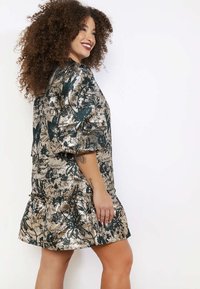 Šaty s krátkym rukávom v A-strihu s metalickým zlatým a tyrkysovým kvetinovým vzorom, s volánkovým lemom a textúrovaným povrchom látky.