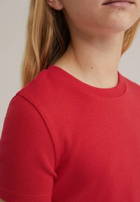 Piros bordázott, rövid ujjú póló kerek nyakkivágással, sima textúrával és testhezálló fazonnal. Nincsenek látható logók vagy minták.