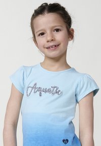 Svijetloplavi majica kratkih rukava s gradijentnim dizajnom, uz riječ "Akvatično" u teksturiranoj izvezenoj tkanini i malim logotipom srca na rubu.