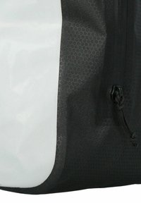 Mochila en blanco y negro con un patrón hexagonal texturizado, que cuenta con un zipper lateral y un cierre de cordón para un acceso ajustable.