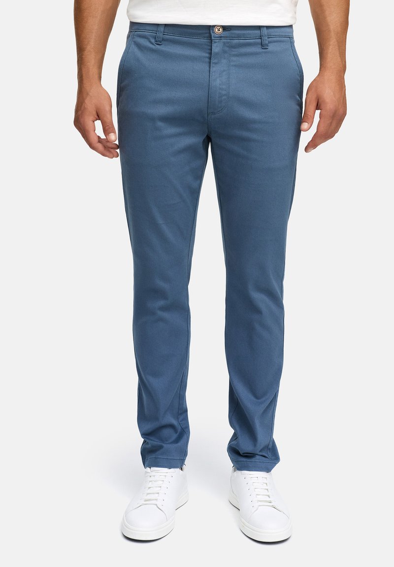 Niebieskie bawełniane chinosy o slim fit, z bocznymi kieszeniami, klasycznym zapięciem na guzik oraz fakturowanym wykończeniem. Stylizowane z białymi sneakersami.