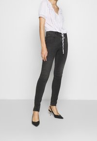 Schmale schwarze Jeans mit mittelhohem Bund, ausgestattet mitFronttaschen und einer dezenten, verblassten Textur. Kombiniert mit einer weißen, bestickten Bluse.