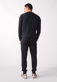 Schwarzes Sweatshirt und Jogginghosen aus weichem Stoff, mit lockerer Passform und gerippten Bündchen. Sneaker fügen einen kontrastierenden metallischen Akzent hinzu.