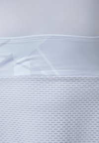 Top desportivo leve em branco, com uma parte superior lisa e uma parte inferior de malha texturizada e respirável, apresentando padrões geométricos subtis.