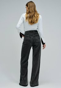 Szerokie szare dżinsowe spodnie z wysokim stanem, kontrastowymi szwami i dwiema tylnymi kieszeniami. Materiał ma miękką teksturę i lekko wyblakłe wykończenie.