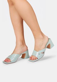 Light blue patent slide sandals with a square toe and chunky heel. Crossed straps and a cutout detail enhance the design.