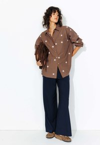 Chemise à rayures brunes avec broderie florale blanche, assortie à un pantalon large à rayures bleu marine et des ballerines à motifs léopard.