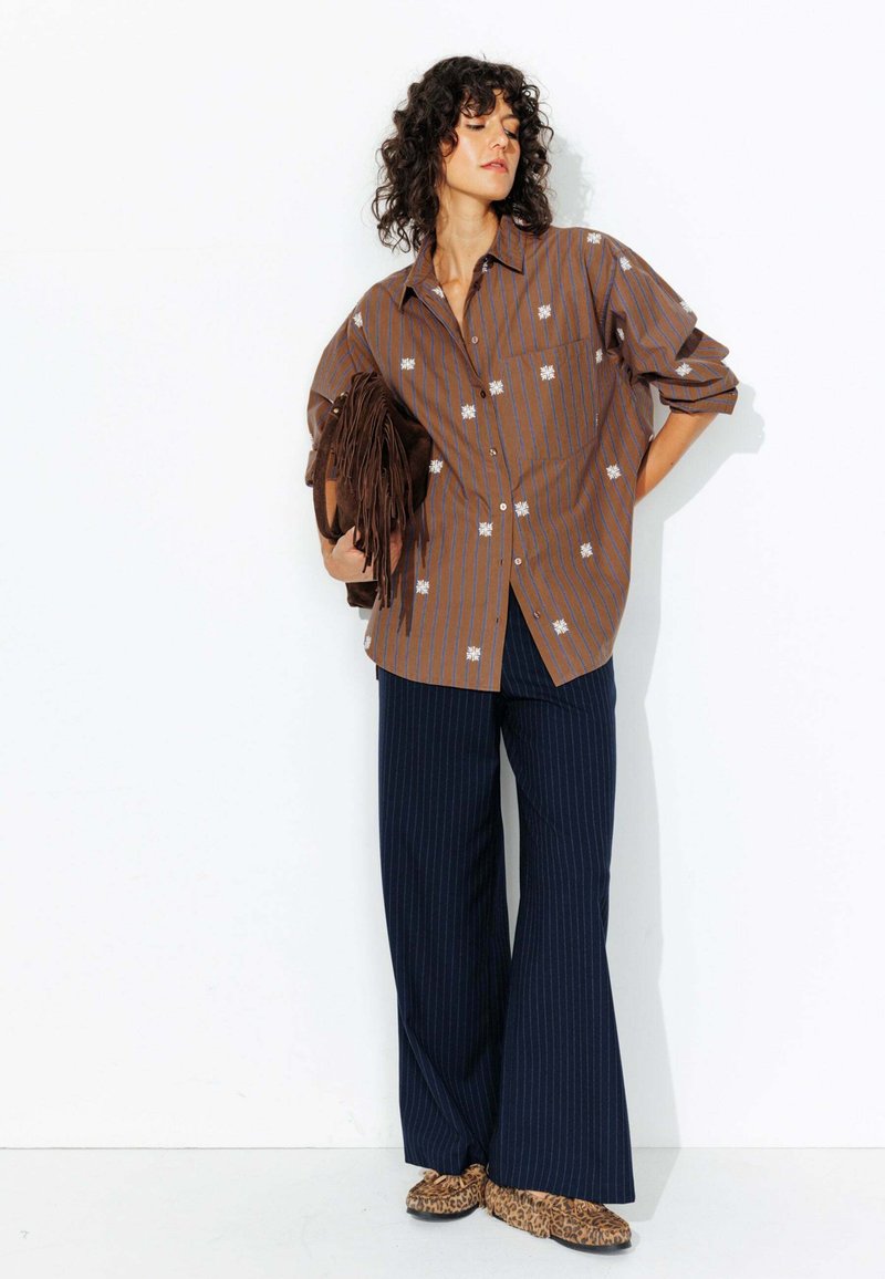 Chemise à rayures brunes avec broderie florale blanche, assortie à un pantalon large à rayures bleu marine et des ballerines à motifs léopard.