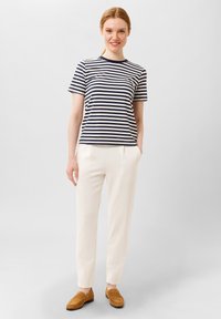 Pruhované námořnické modré a bílé tričko s kulatým výstřihem, spárované s krémovými zúženými kalhotami. Dokončeno hnědými mokasínami. Hladký materiál.