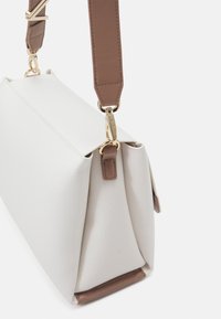 Borsa bianca strutturata con una forma rigida, caratterizzata da una tracolla marrone e dettagli in hardware dorato.