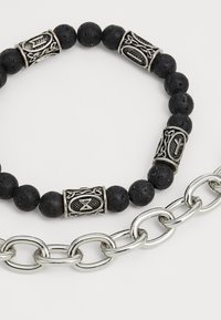 Bracelet en perles noires avec des intercalaires décoratifs en argent et une chaîne en argent connectée. Les perles ont une finition texturée et mate.